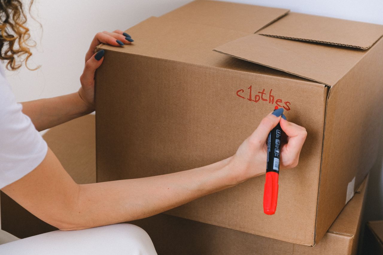 services-07 Gros plan d’une femme étiquetant une boîte en carton avec un marqueur rouge à l’intérieur.